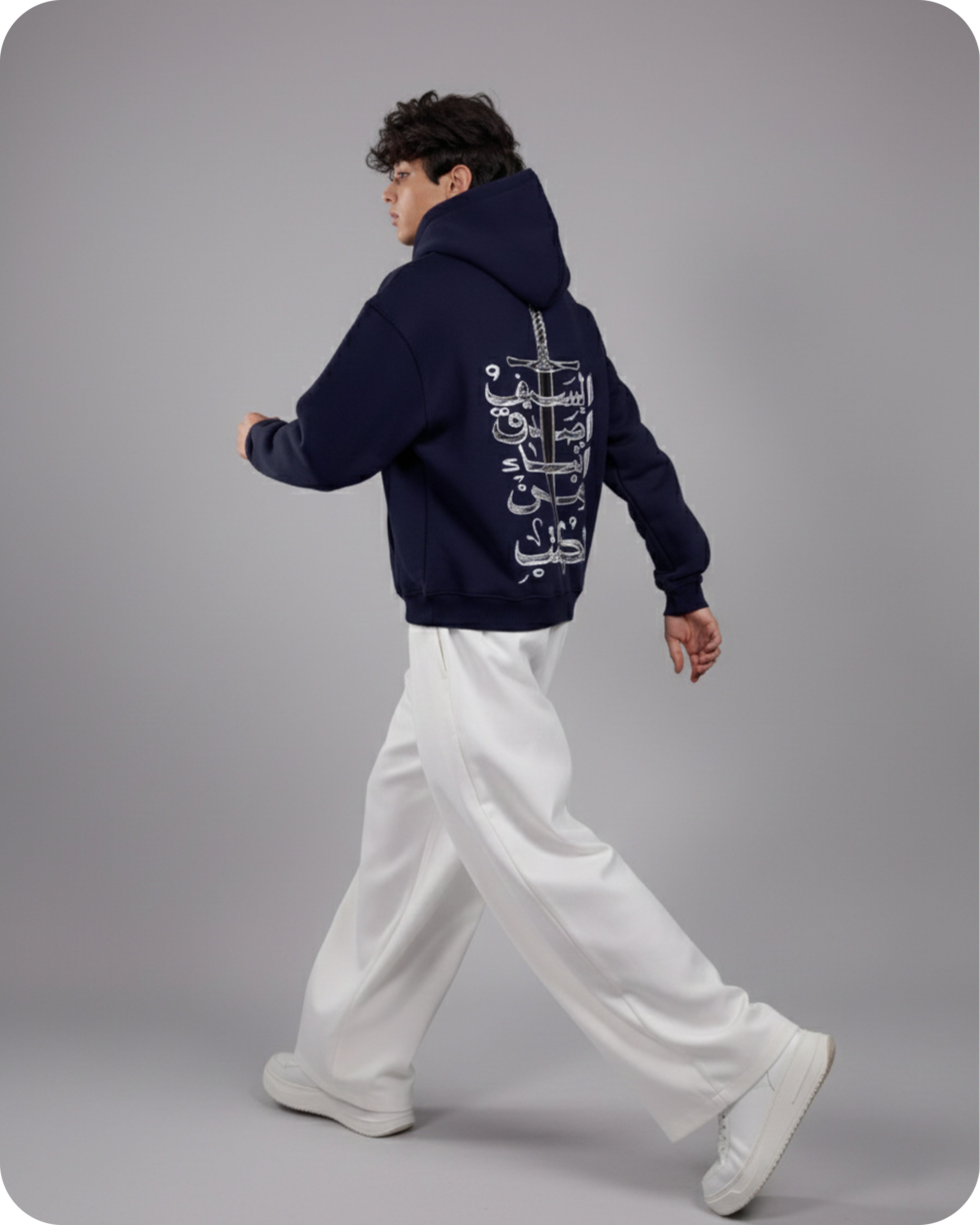 Person wearing a navy hoodie with a white graphic on the back, walking on a gray background
