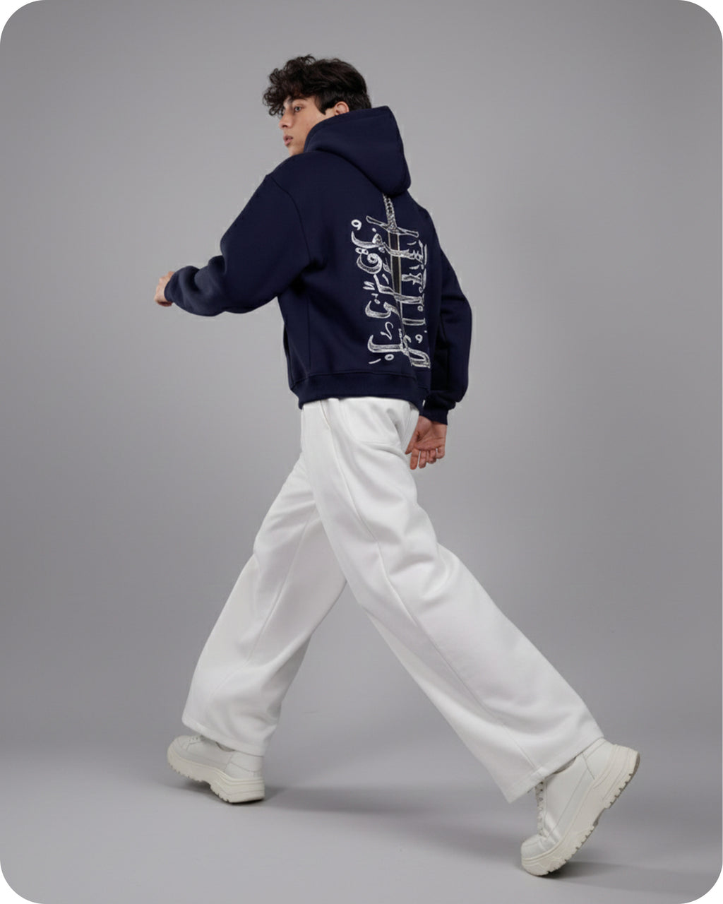 Person wearing a navy hoodie with white text and white pants on a gray background