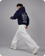 Person wearing a navy hoodie with white text and white pants on a gray background