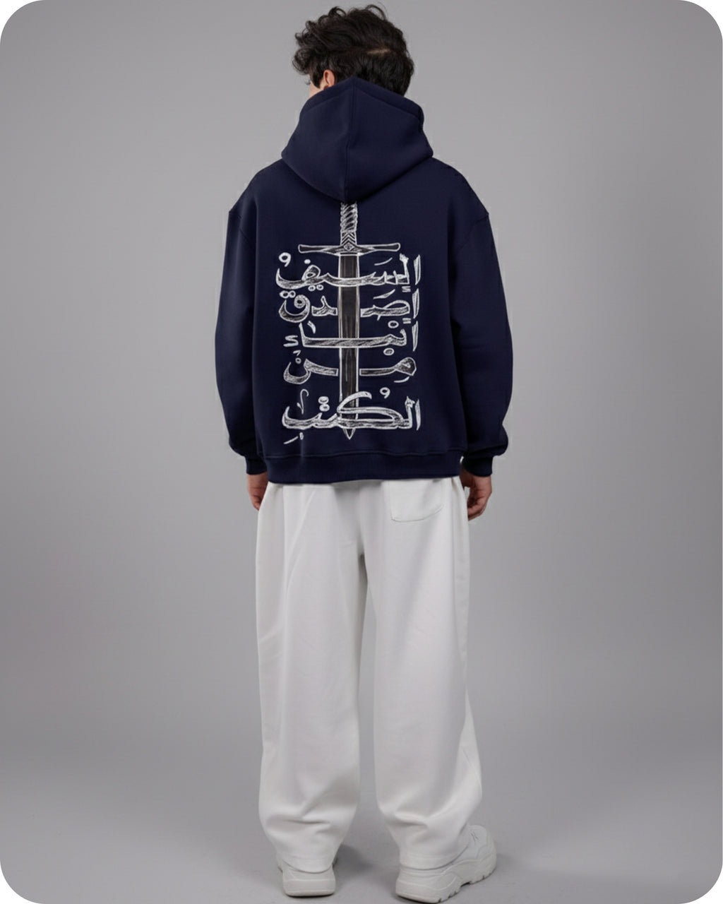 Person wearing a navy hoodie with Arabic text and a sword design on the back, standing against a gray background.