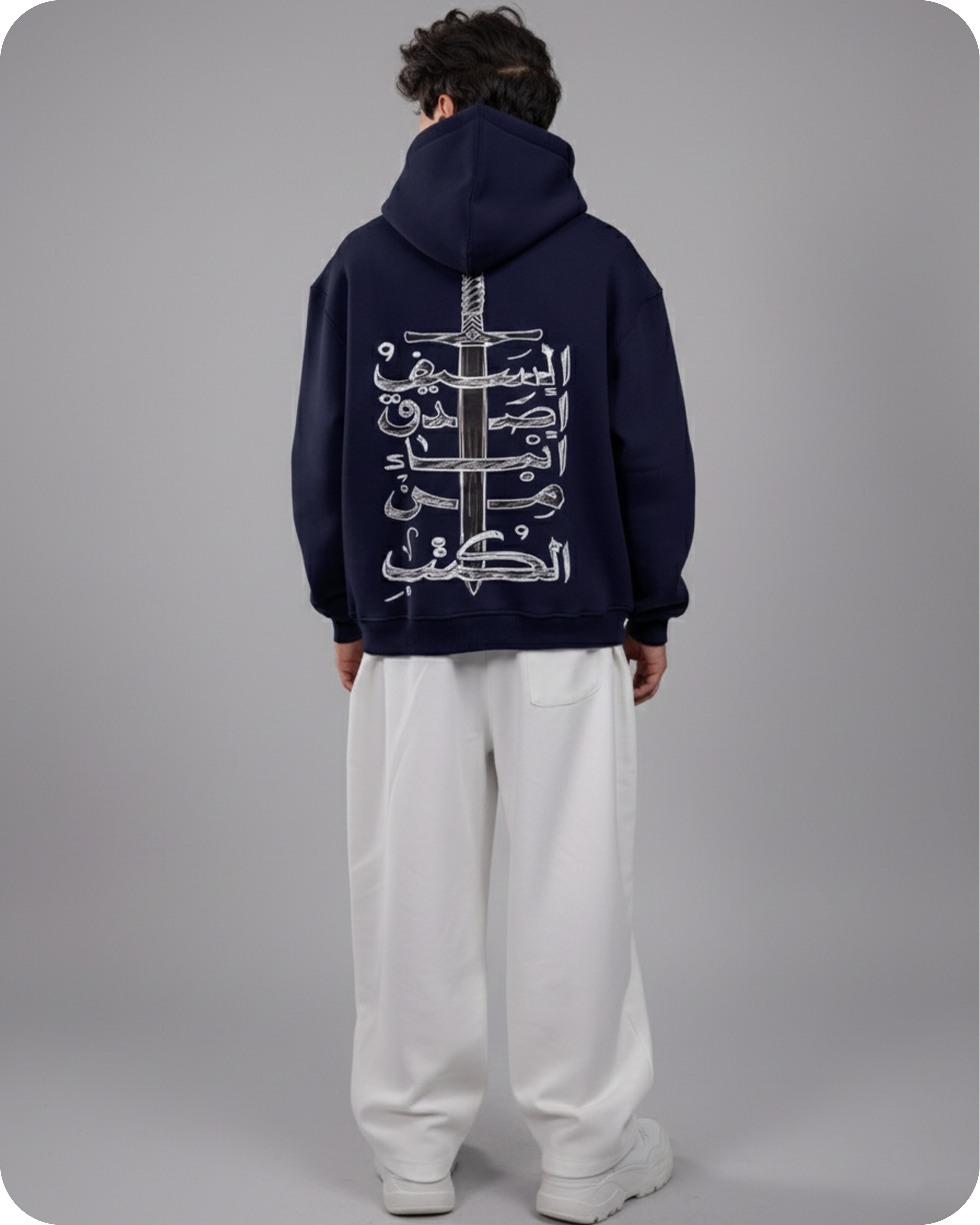 Person wearing a navy hoodie with Arabic text and a sword design on the back, standing against a gray background.