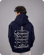 Person wearing a navy hoodie with white Arabic calligraphy design on the back against a gray background