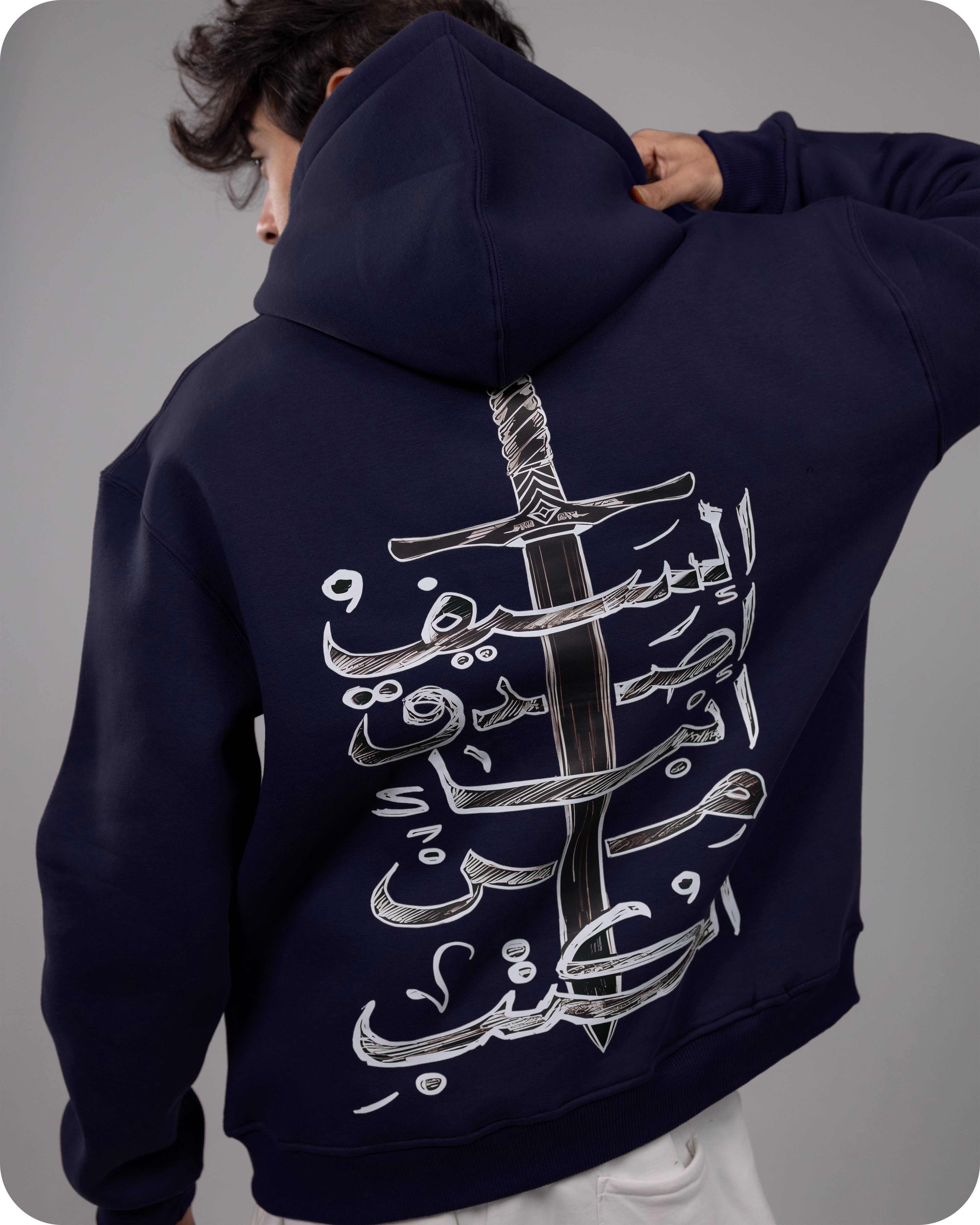 Navy hoodie with white Arabic calligraphy design on the back, worn by a person against a gray background.