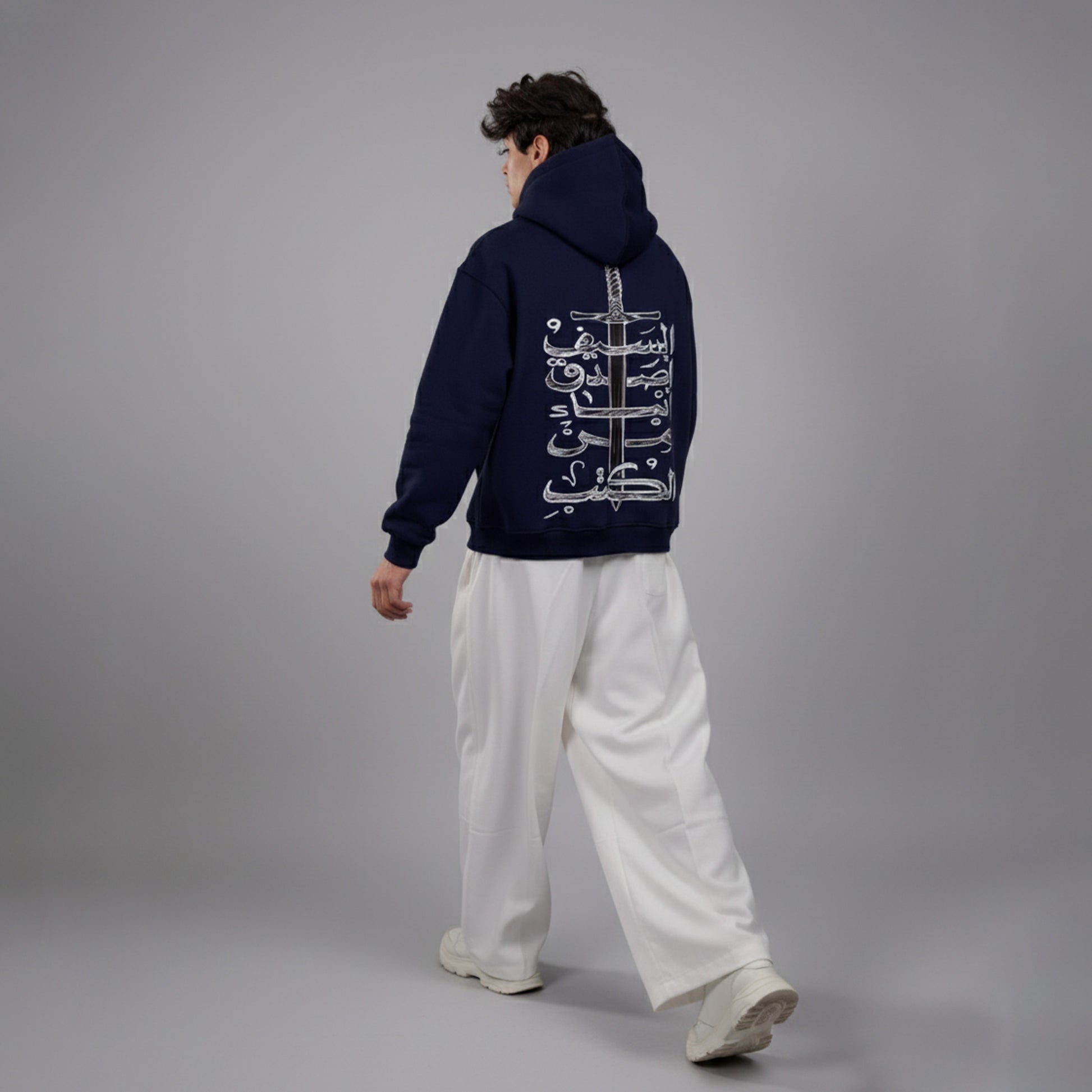 Person wearing a navy hoodie with white text on the back, standing against a gray background