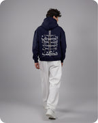 Person wearing a dark blue hoodie with white Arabic text on the back, standing against a gray background.