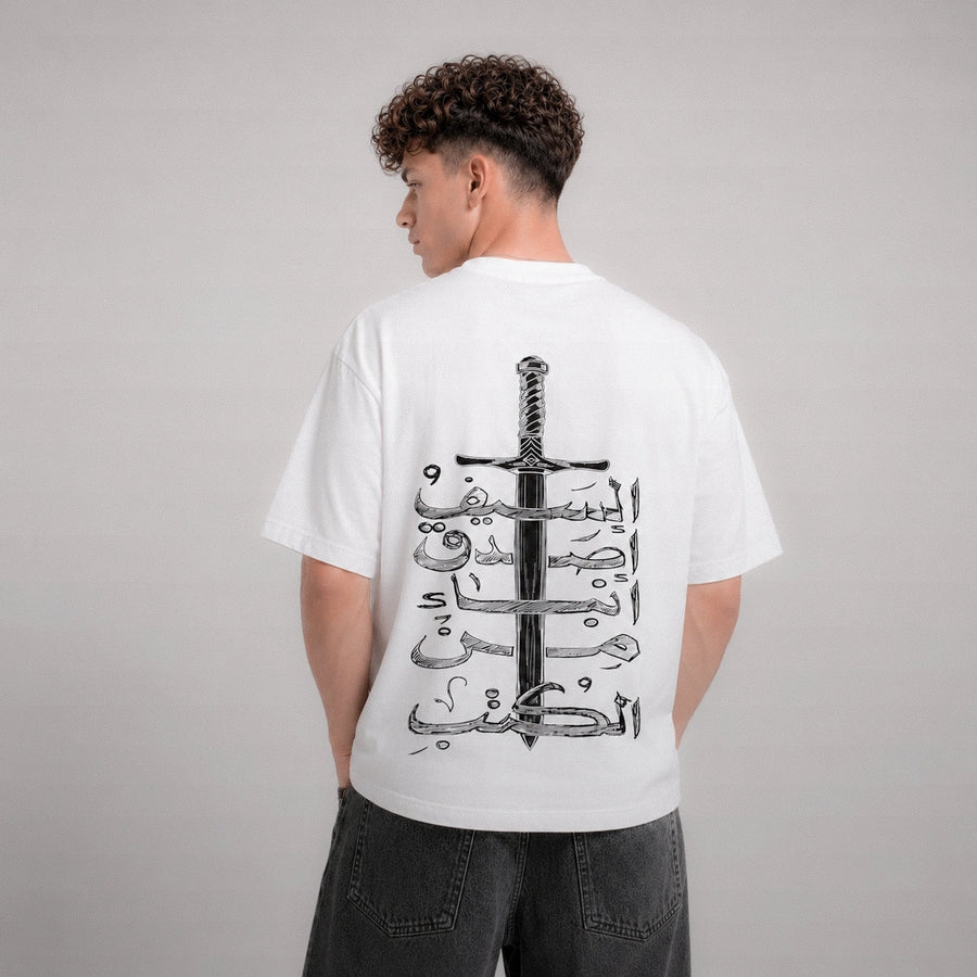 Person wearing a white t-shirt with a black sword and Arabic text design on the back, standing against a gray background.