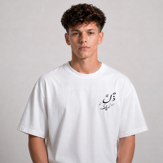 Person wearing a white t-shirt with Arabic text on a plain background