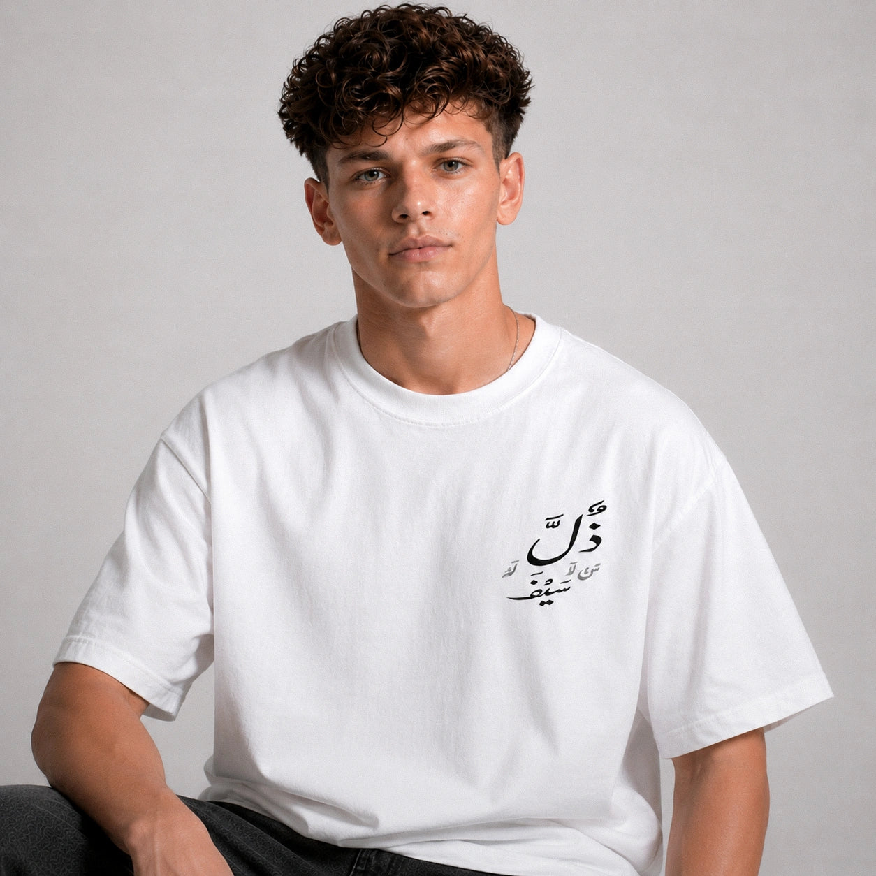 Person wearing a white t-shirt with Arabic text on a plain background
