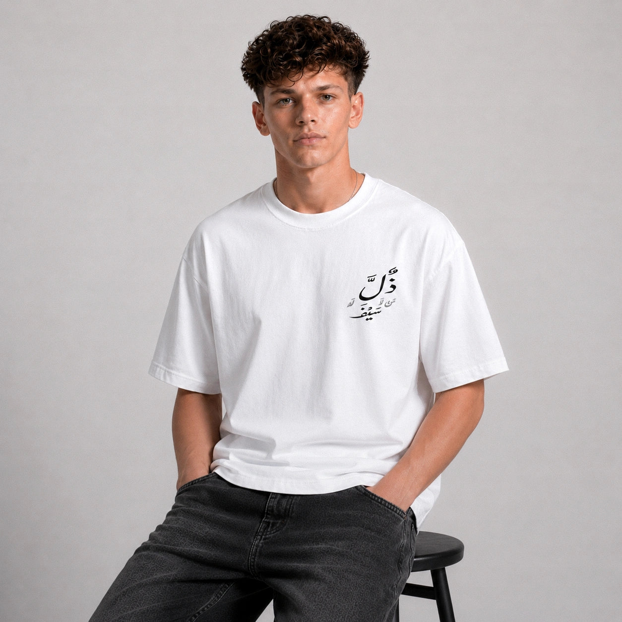 Person wearing a white t-shirt with Arabic text on a gray background