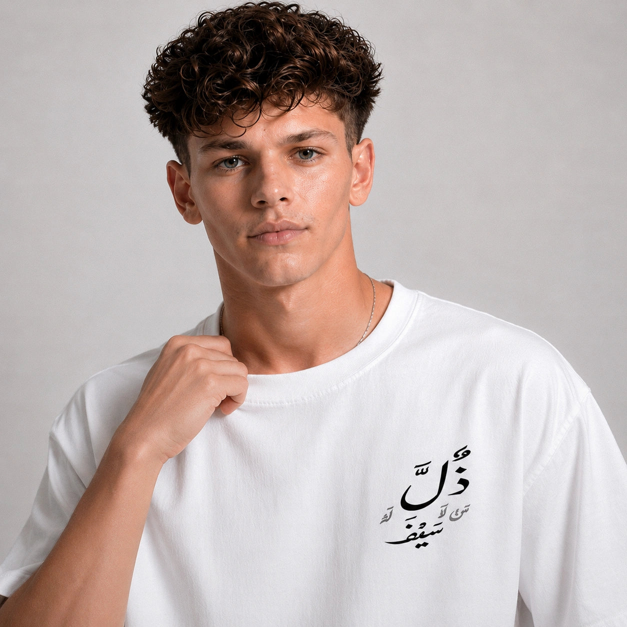 Man wearing a white t-shirt with Arabic text on a gray background