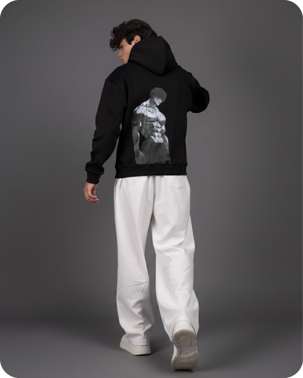 Person wearing a black hoodie with a graphic design on the back, standing against a gray background