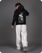 Person wearing a black hoodie with a graphic design on the back, standing against a gray background