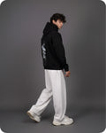 Person wearing a black hoodie with white graphics and white pants on a gray background