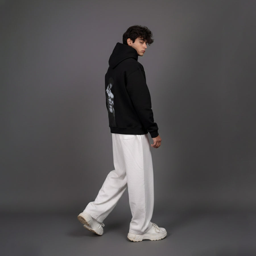 Person wearing a black hoodie with white graphics and white pants on a gray background