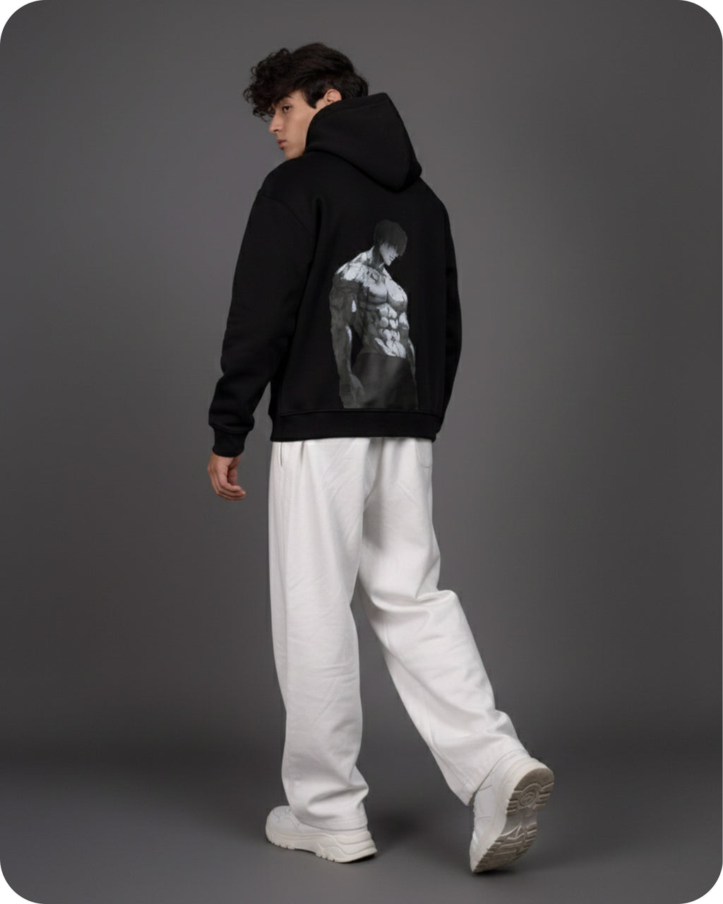 Person wearing a black hoodie with a graphic design on the back, standing against a gray background