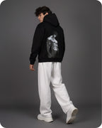 Person wearing a black hoodie with a graphic design on the back, standing against a gray background