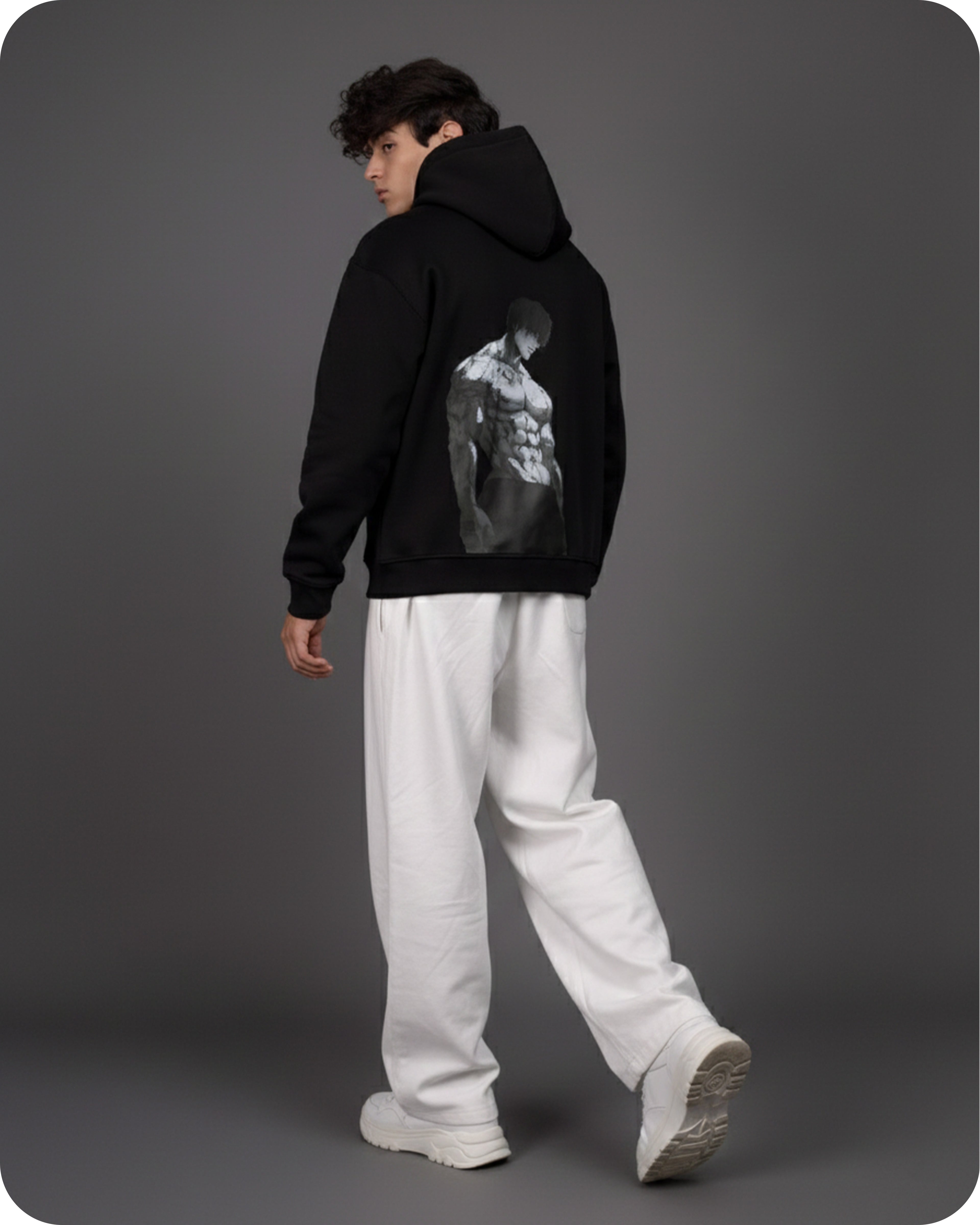 Person wearing a black hoodie with a graphic design on the back, standing against a gray background