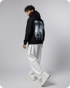 Person wearing a black hoodie with a graphic design on the back, standing against a plain background