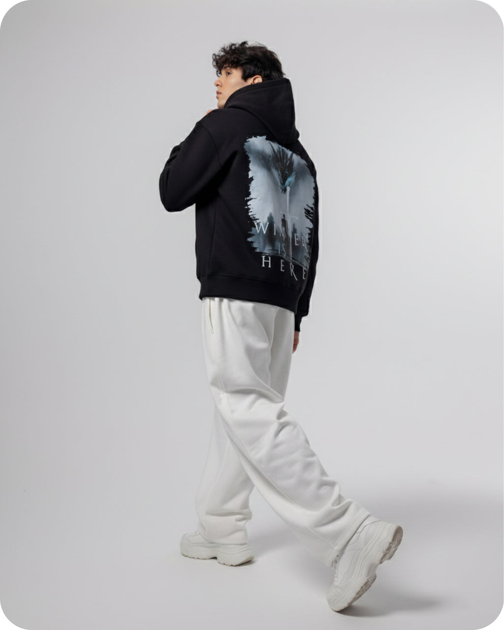 Person wearing a black hoodie with a graphic design on the back, standing against a white background