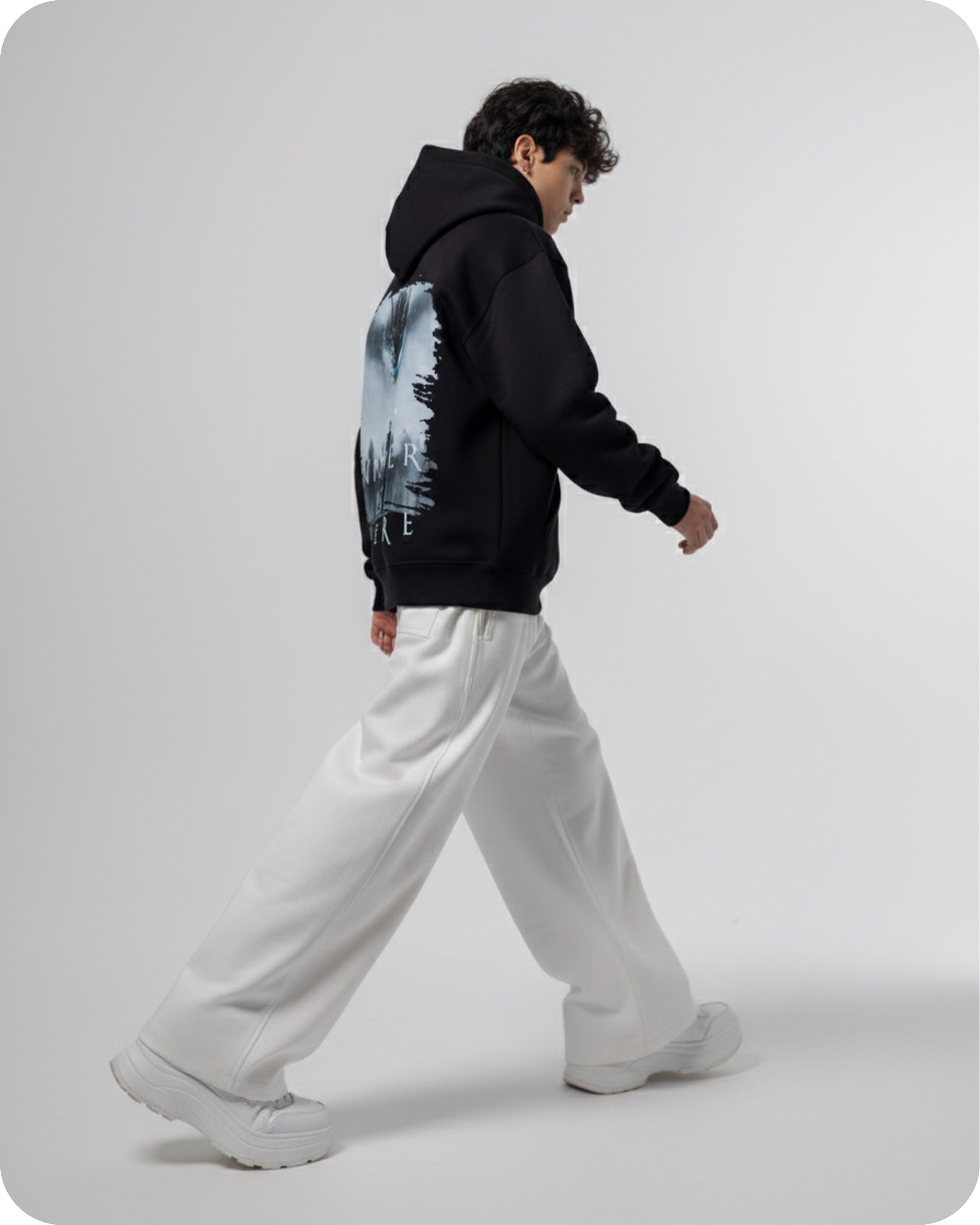 Person wearing a black hoodie with a nature graphic and white pants on a light gray background