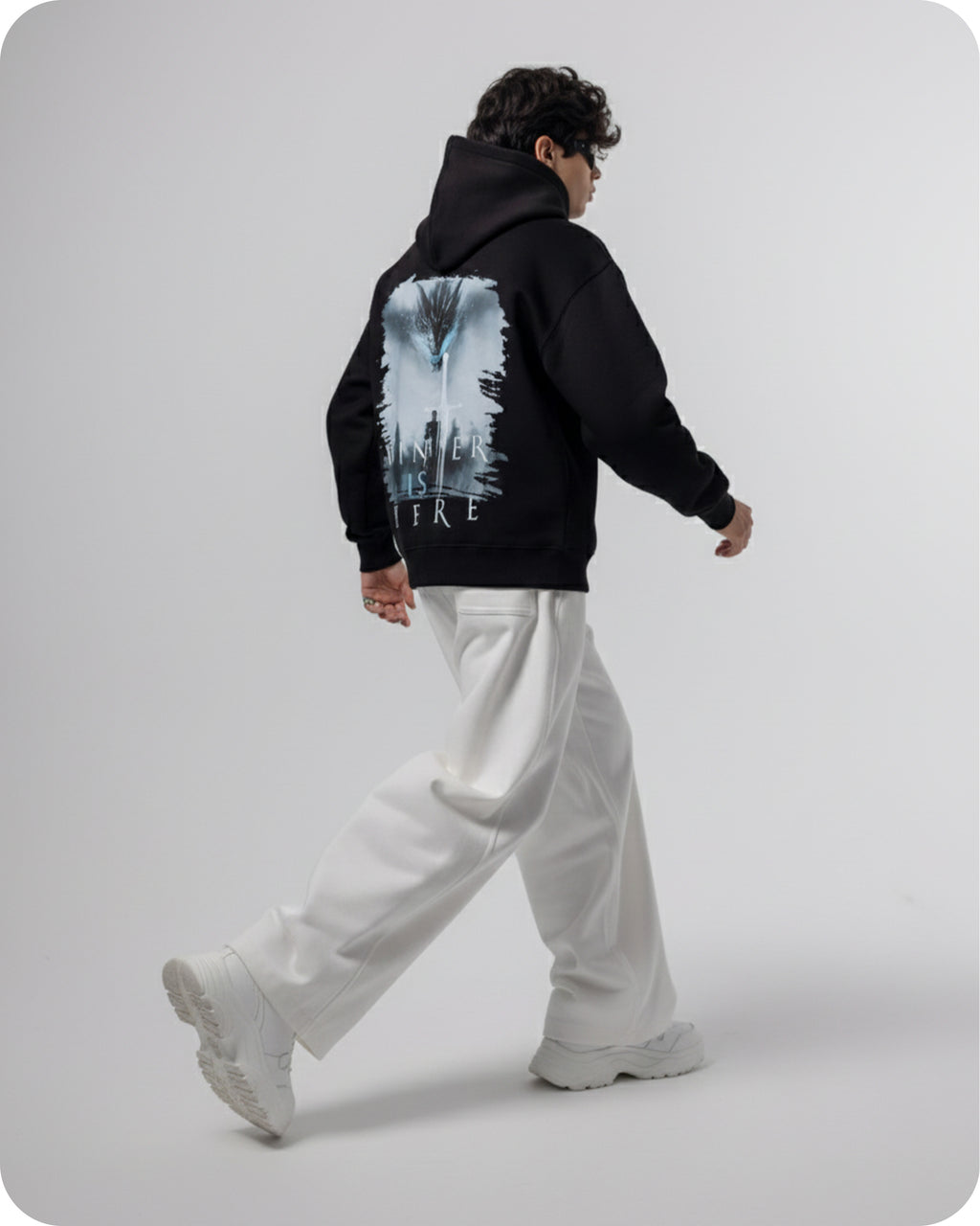 Person wearing a black hoodie with a graphic design on the back, standing against a plain background