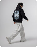 Person wearing a black hoodie with a graphic design on the back, standing against a plain background