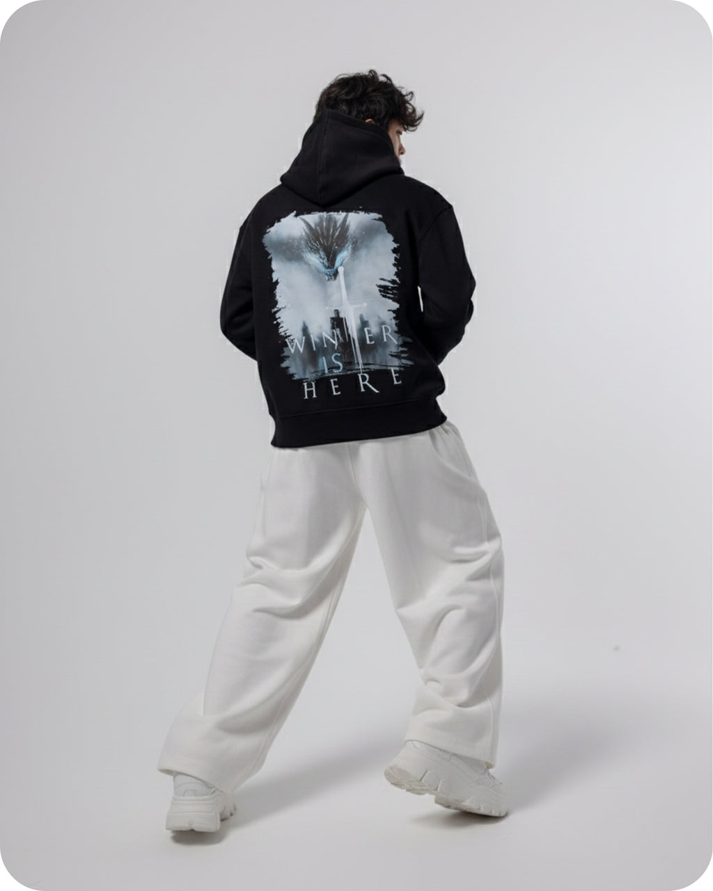 Person wearing a black hoodie with a graphic design on the back, standing against a white background
