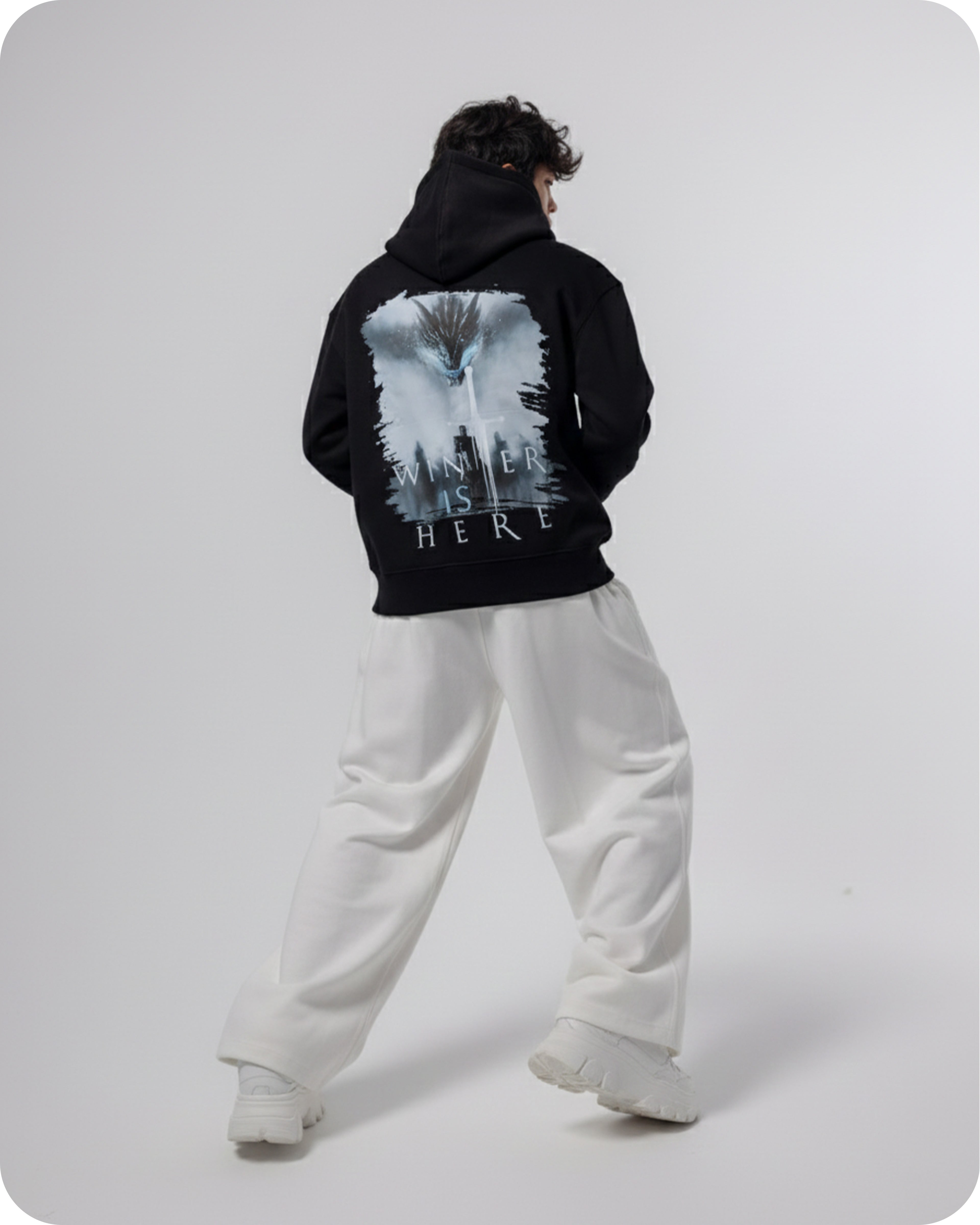 Person wearing a black hoodie with a graphic design on the back, standing against a white background