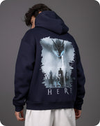 Person wearing a navy hoodie with a graphic design on the back against a gray background