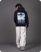 Person wearing a navy hoodie with a graphic design on the back against a gray background