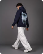 Person wearing a navy hoodie with a graphic design on the back, walking against a gray background