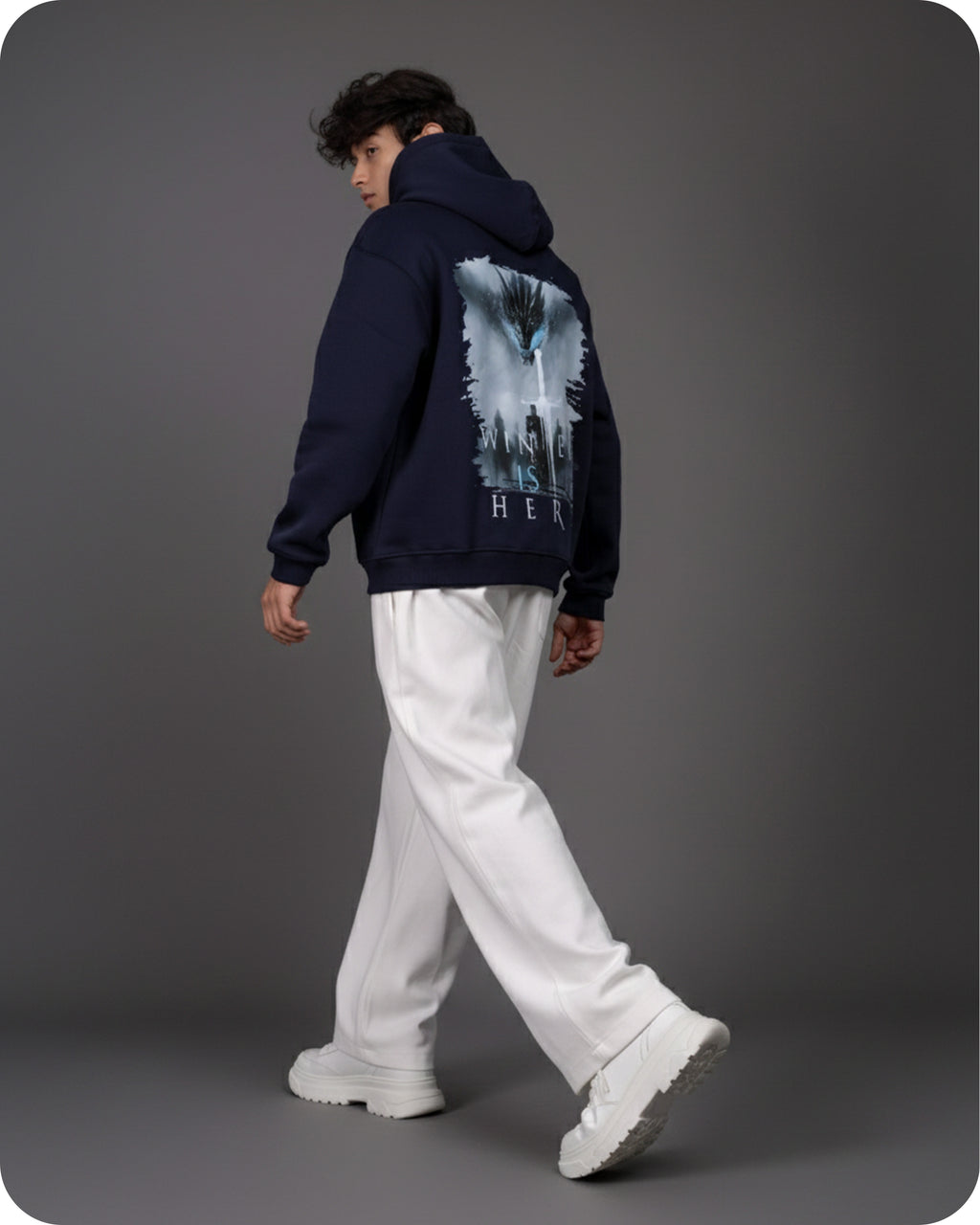 Person wearing a navy hoodie with a graphic design on the back, walking against a gray background