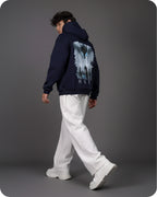 Person wearing a navy hoodie with a graphic design on the back, walking against a gray background