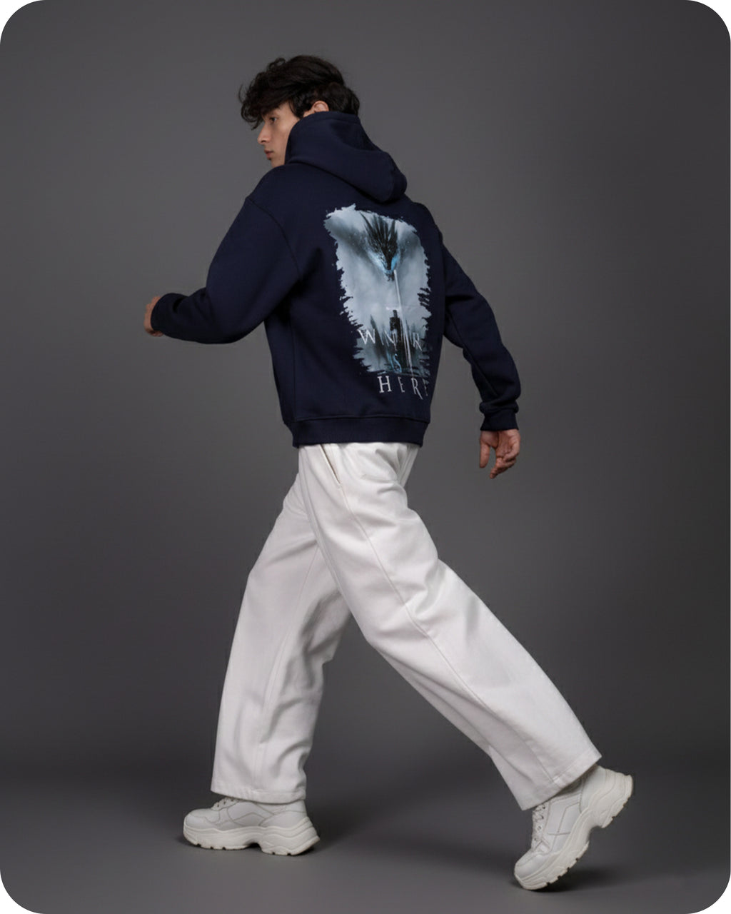 Person wearing a navy hoodie with a graphic design on the back, walking against a gray background