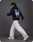 Person wearing a navy hoodie with a graphic design on the back, walking against a gray background