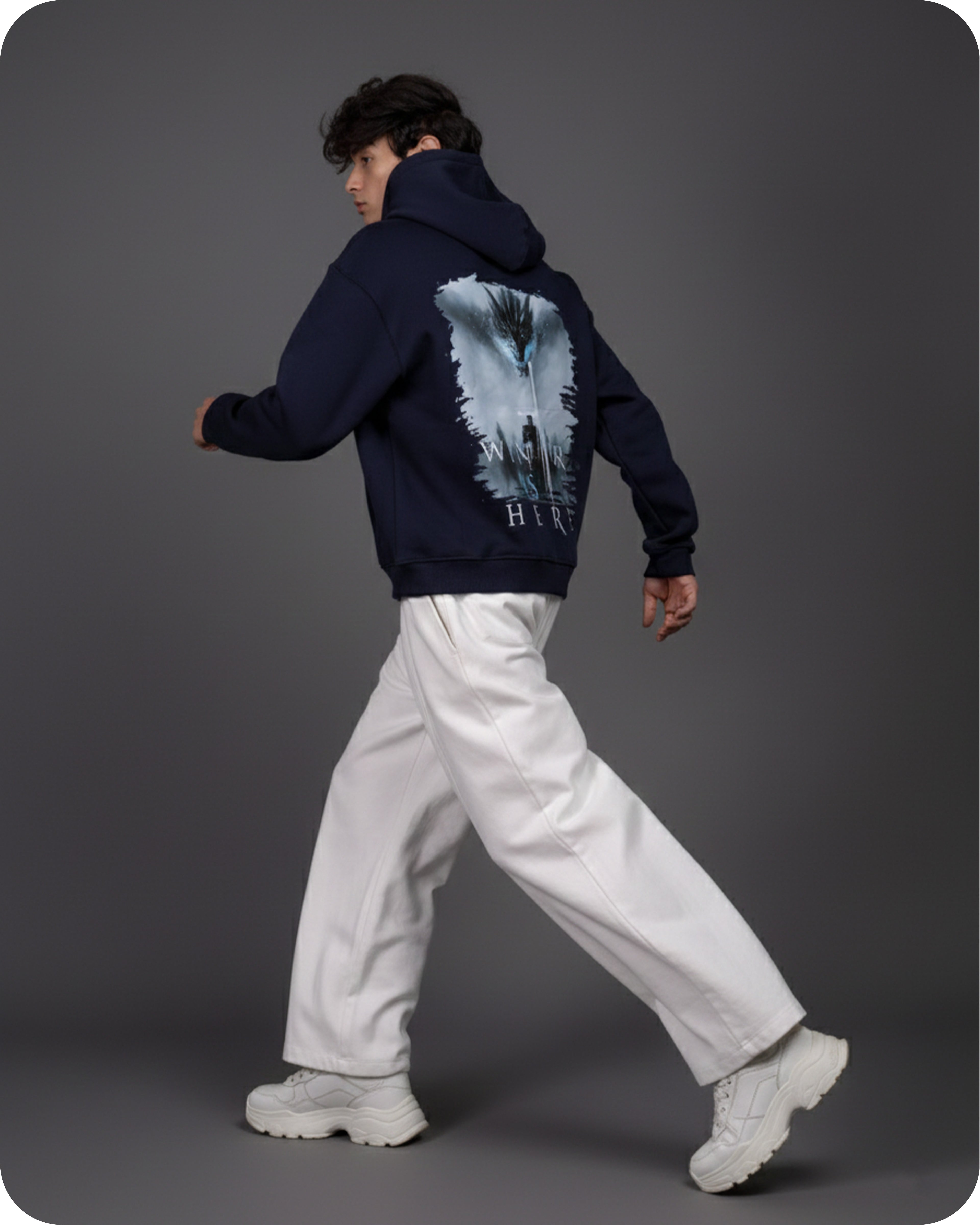 Person wearing a navy hoodie with a graphic design on the back, walking against a gray background